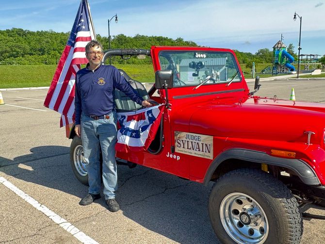 Judge Sylvain standing beside a red Jeep with patriotic decorations and an American flag