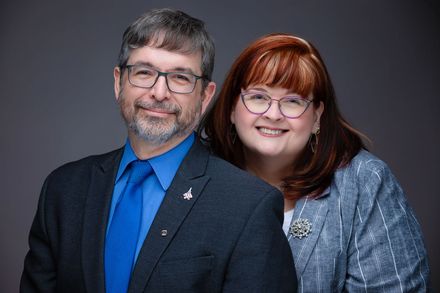 Smiling couple Judge Sylvain and his wife Tina posing against a gray studio backdrop.