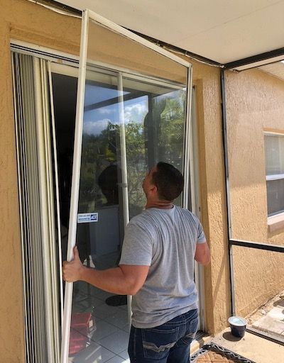 Man holds a white screen door frame, possibly installing or removing it, near a sliding glass door.