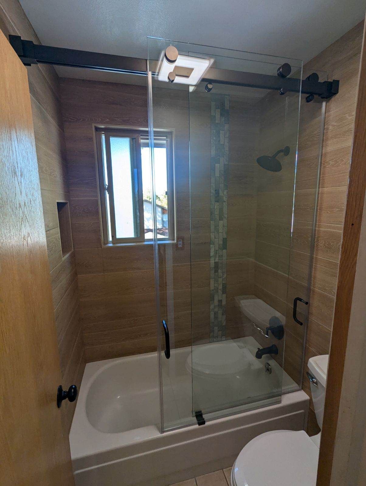 Bathroom with shower/tub combo, sliding glass door, tan tile walls, small window.