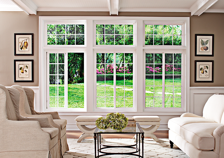 Living room with large windows overlooking a green yard, white furniture, and framed art.