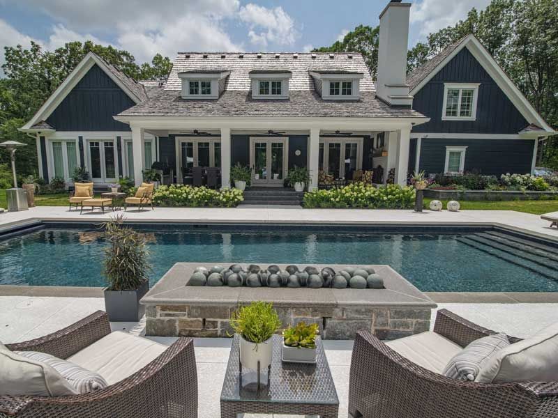 Luxury house with pool, fire pit, and patio seating under a bright sky