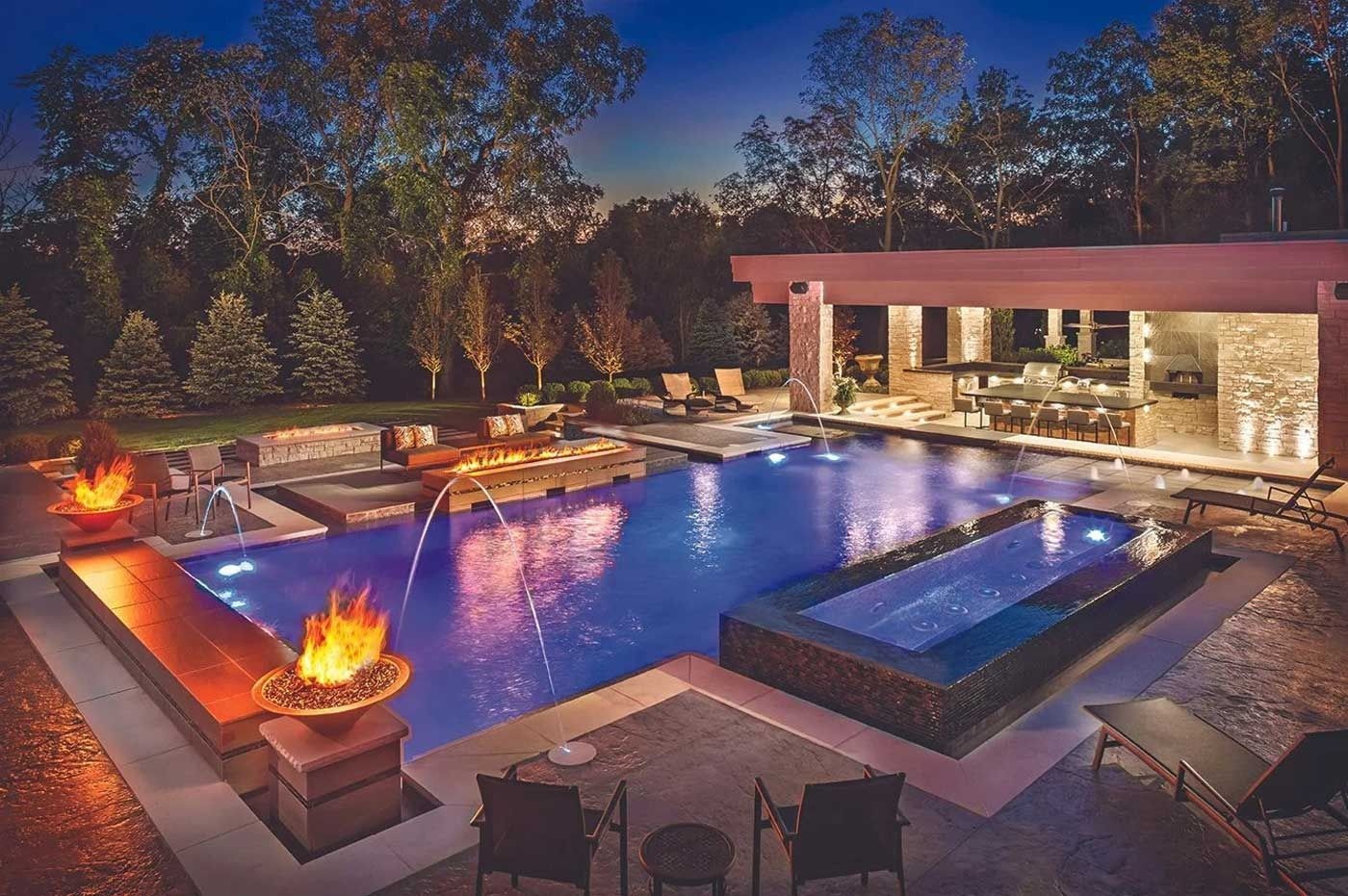 Luxury backyard pool at dusk with fire bowls, spa, and modern patio seating