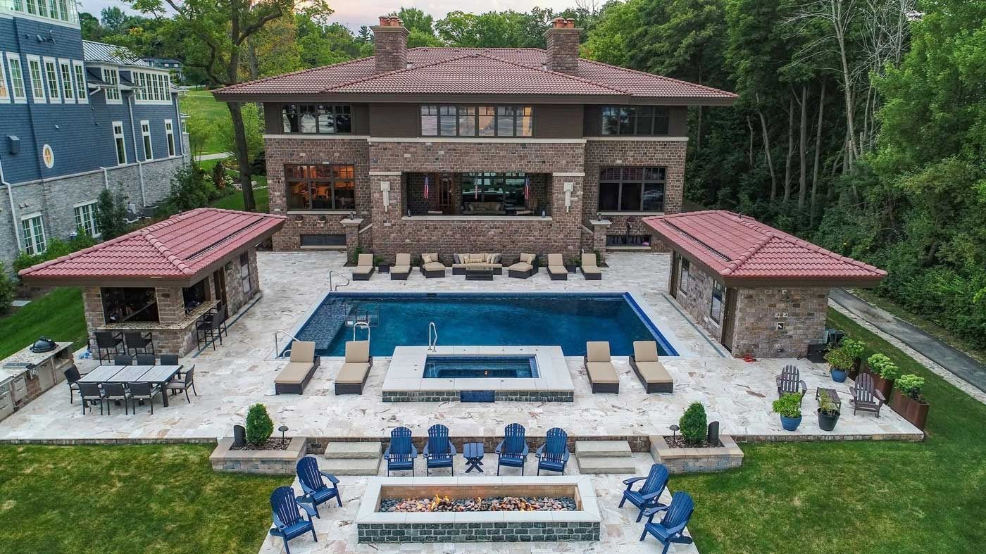 Aerial view of a large stone house with a central pool, patio seating, and two red-roofed pavilions