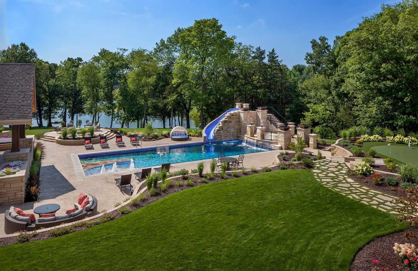 Resort-style outdoor pool with blue water, rock waterfall, lounge chairs, and green lawn under trees