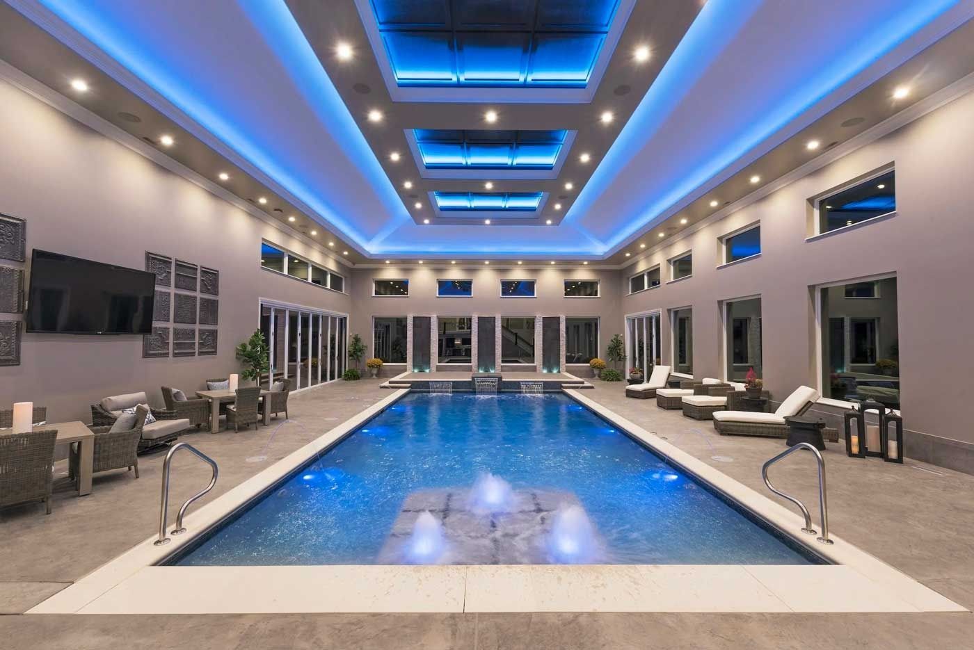 Indoor pool in a modern spa with blue-lit ceiling and lounge chairs surrounding the water