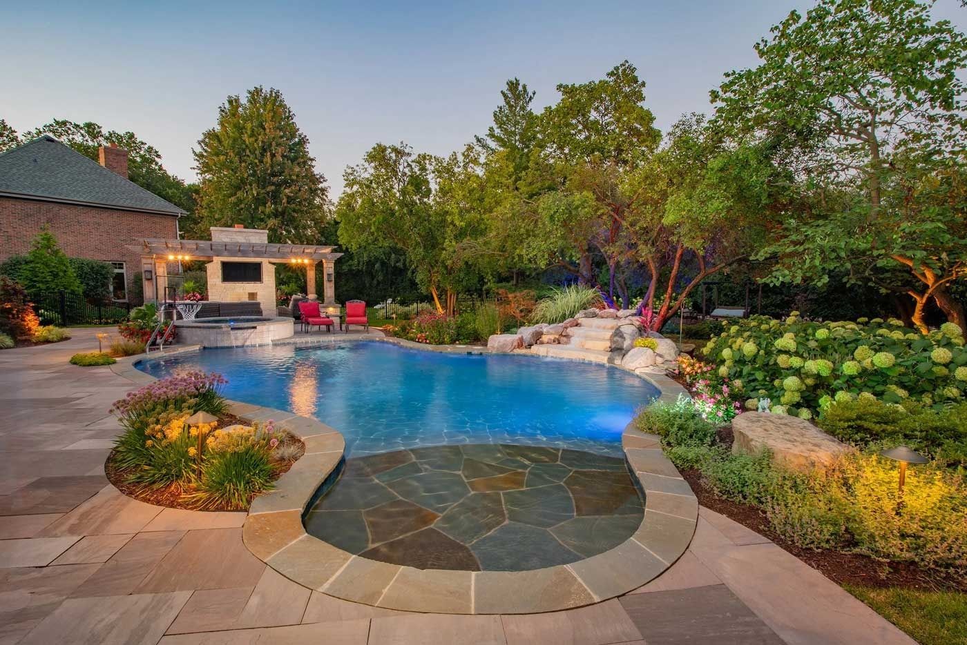 Backyard pool with stone patio, landscaped garden, and a patio pavilion at sunset