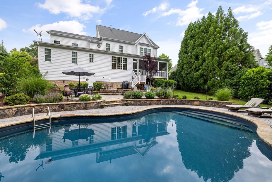 White house with a backyard swimming pool and patio under a blue sky