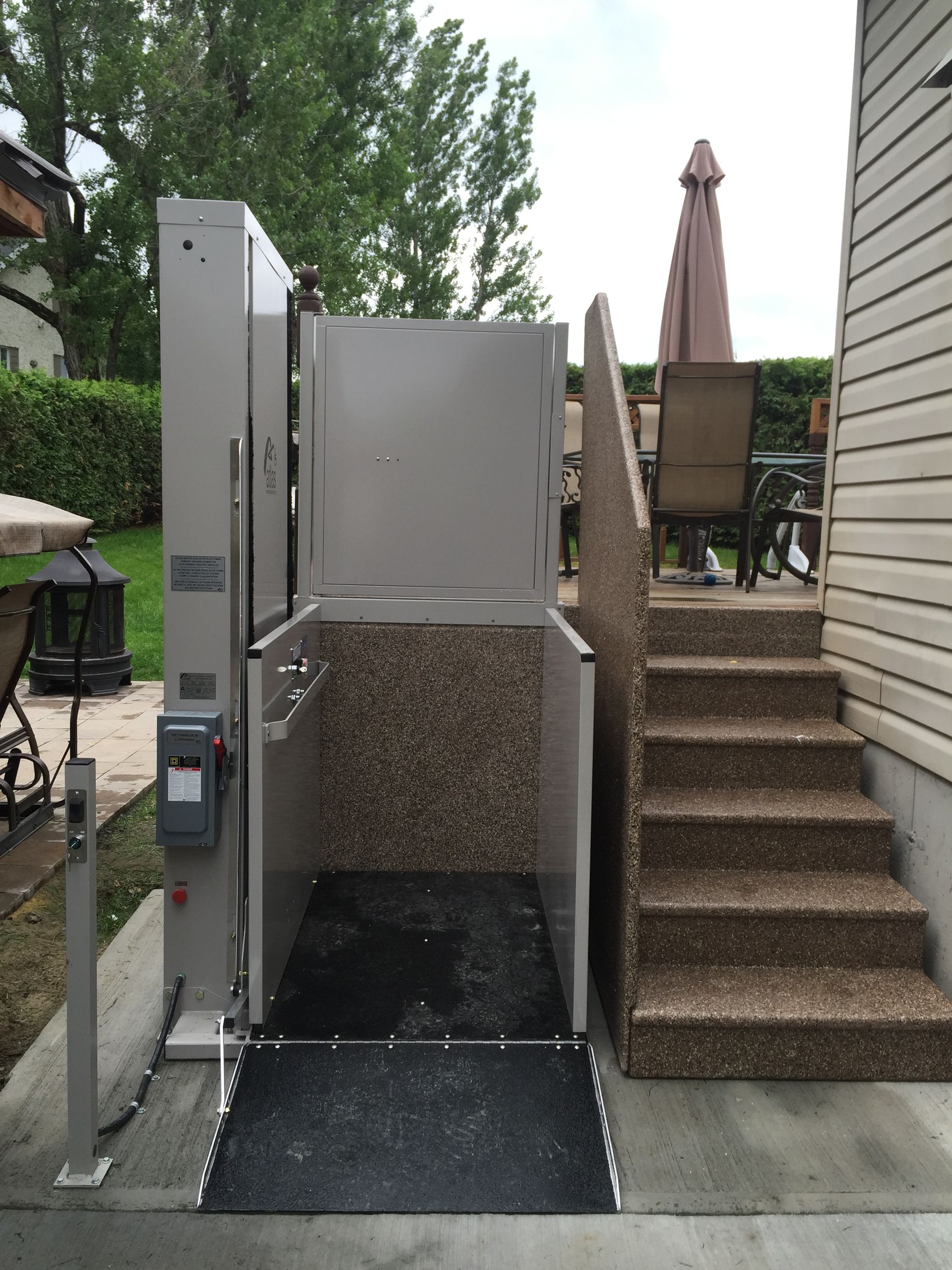 Escalier extérieur et ascenseur pour fauteuil roulant à côté d'une terrasse, donnant accès à une terrasse surélevée.
