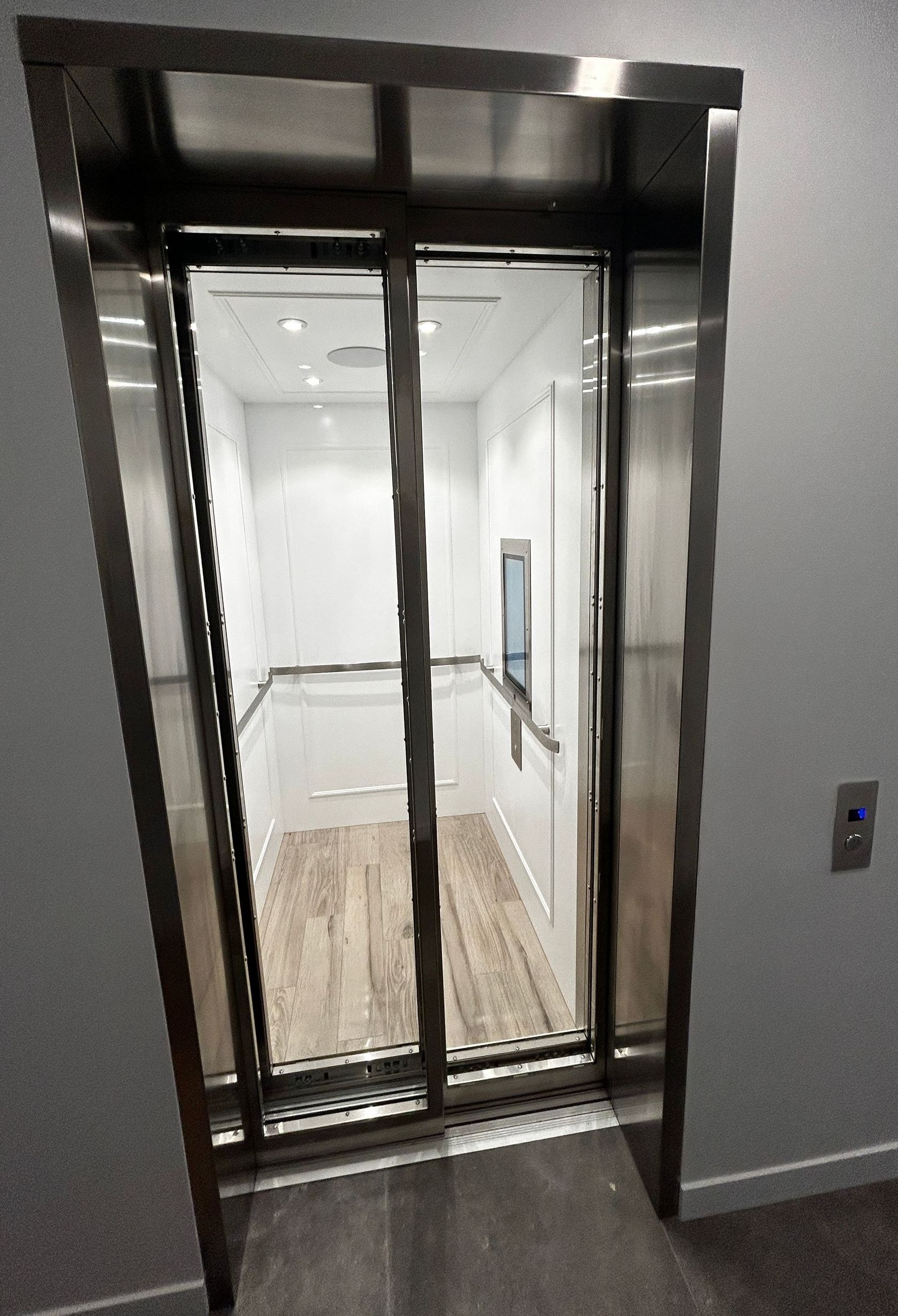 Ascenseur ouvert avec portes vitrées, dévoilant un intérieur lumineux et un sol imitation bois.