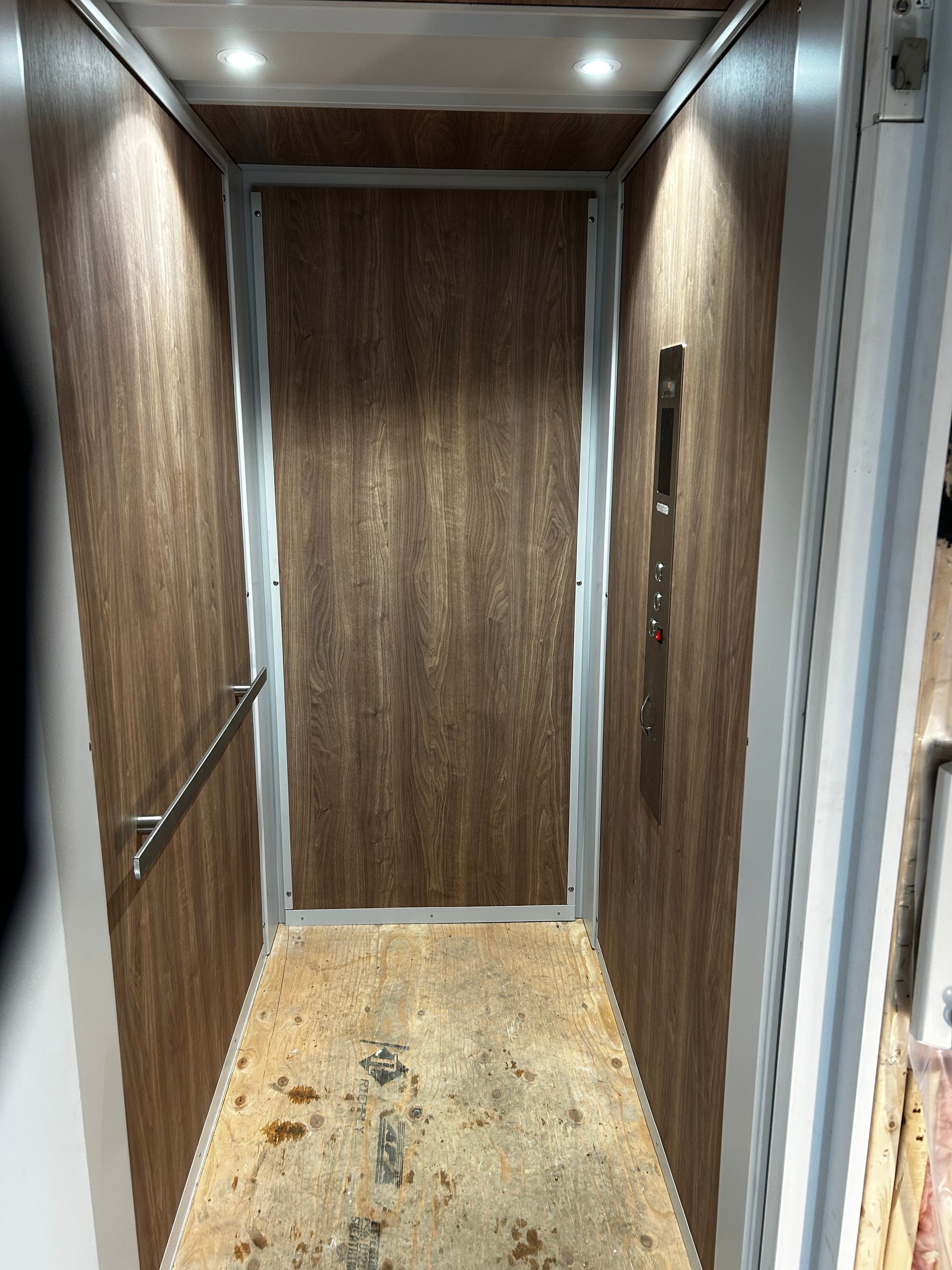 Intérieur d'ascenseur lambrissé, rails en acier inoxydable et sol usé.