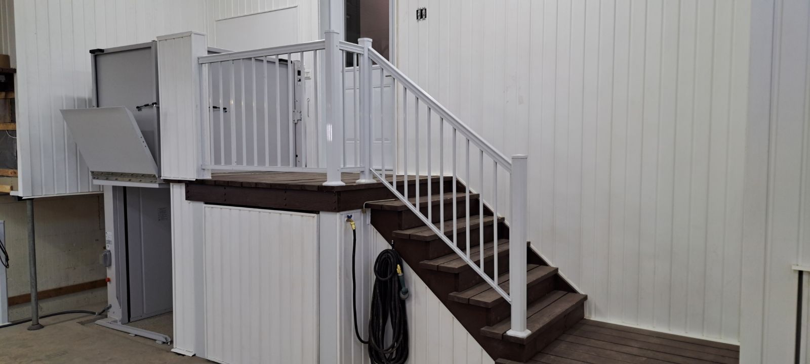 Escalier extérieur en métal avec rampes blanches menant à une plateforme surélevée à côté d'un bâtiment