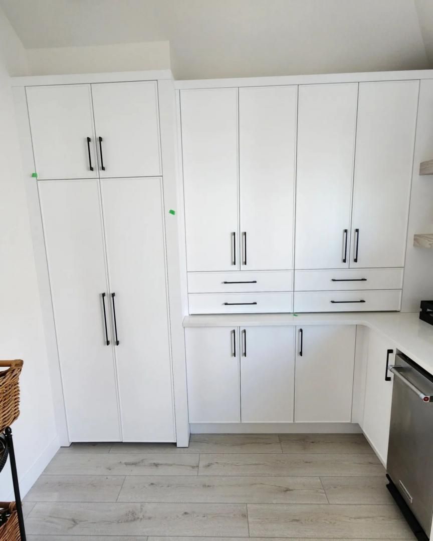 Cuisine équipée de placards blancs à poignées noires et parquet clair, vue du centre de la pièce