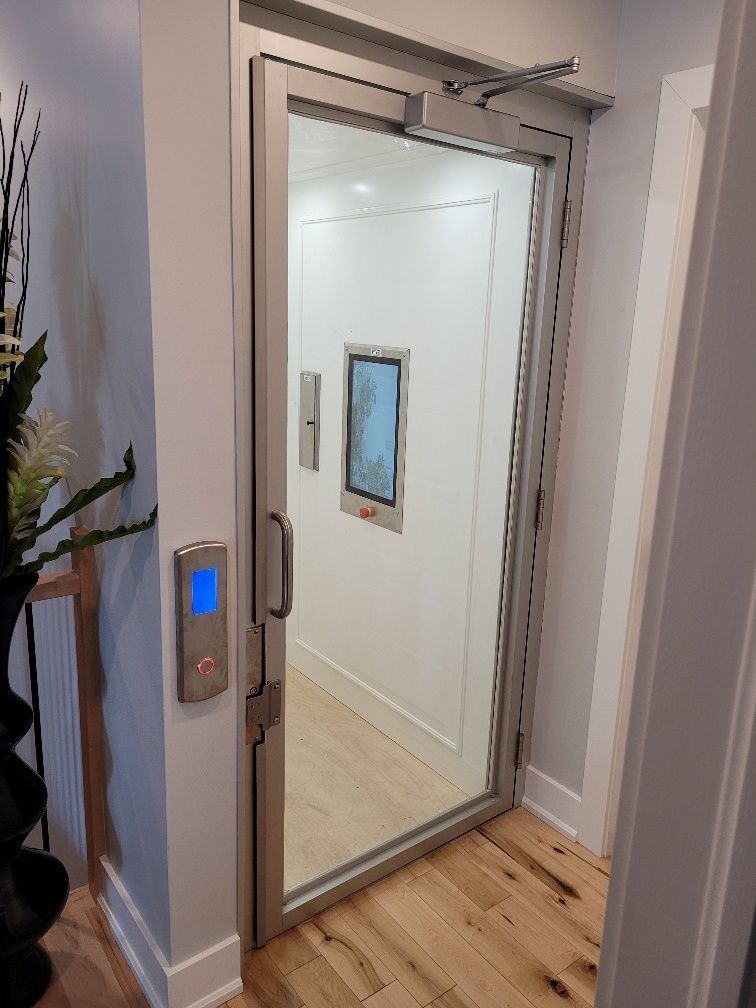 Porte d'ascenseur ouverte avec bouton d'appel éclairé en bleu dans un couloir avec parquet et œuvres d'art murales