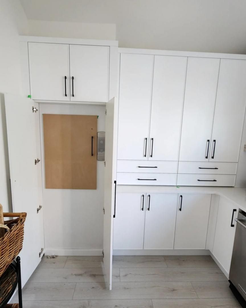 Mur de cuisine blanc avec placards intégrés, porte en bois et carrelage gris clair au sol