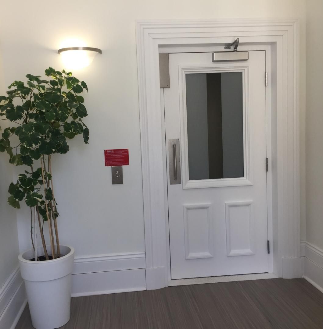 Porte intérieure blanche avec fenêtre à côté d'une plante en pot et d'une applique murale dans un couloir
