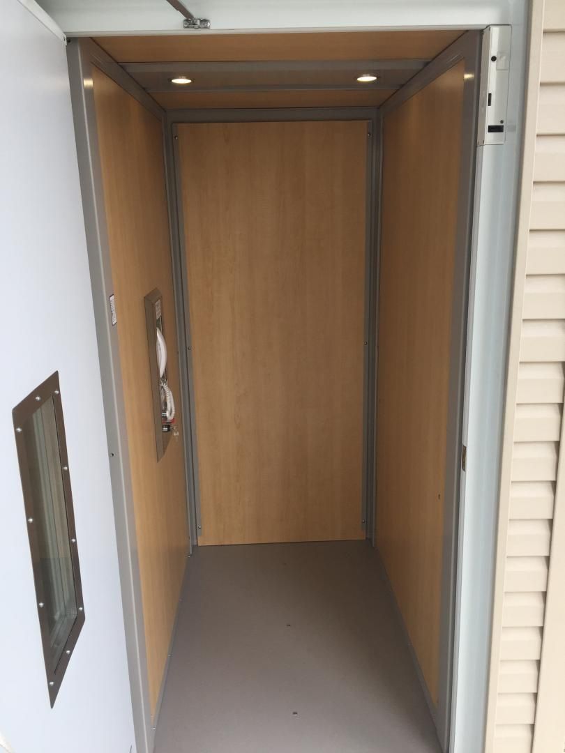 Porte en bois ouverte donnant sur une petite pièce vide au sol beige et aux murs lambrissés.