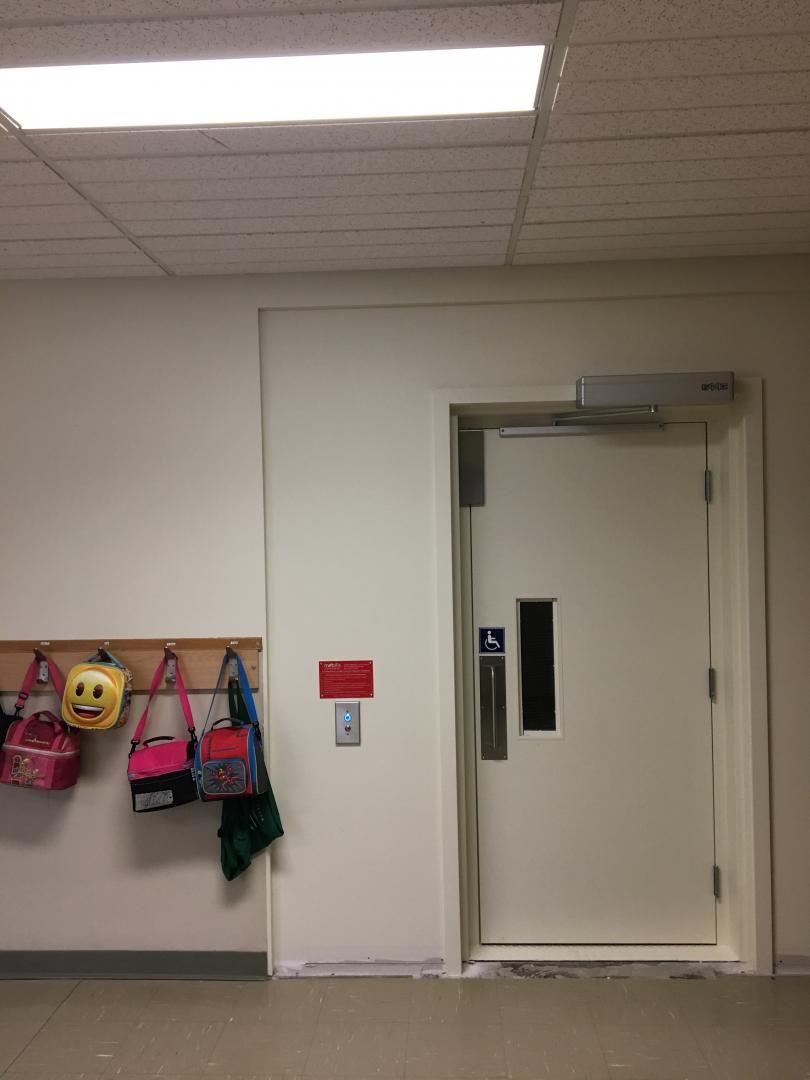 Couloir d'école avec une porte blanche, des patères et des sacs colorés accrochés au mur