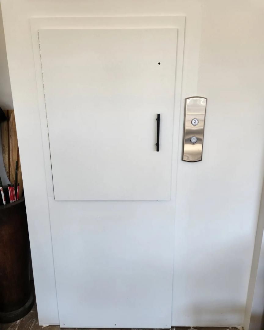 Porte d'armoire murale blanche avec poignée noire à côté d'un panneau de commande mural dans un couloir