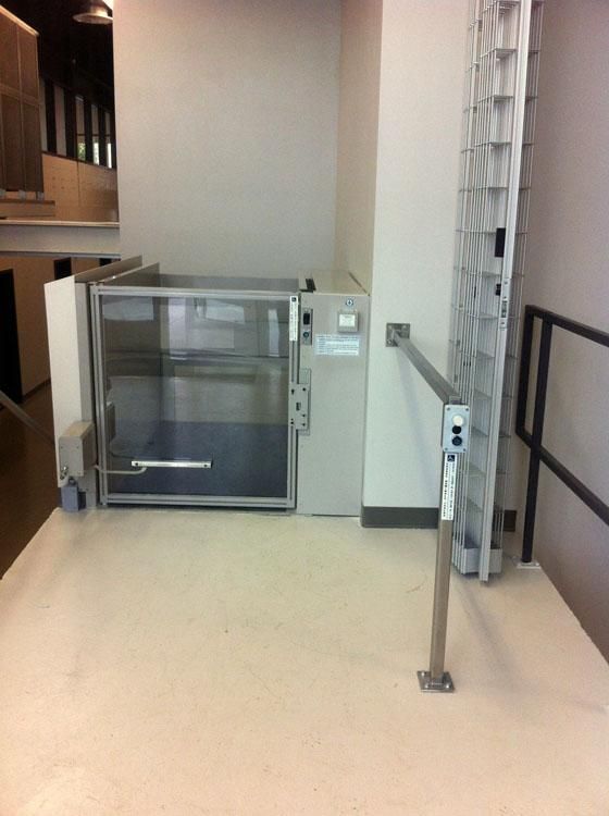 Ascenseur intérieur pour personnes à mobilité réduite à côté d'un escalier, avec rampes métalliques et sol beige