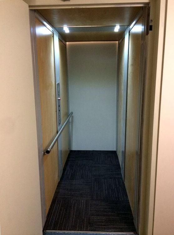 Couloir étroit avec murs lambrissés, sol recouvert de moquette et rampes des deux côtés.