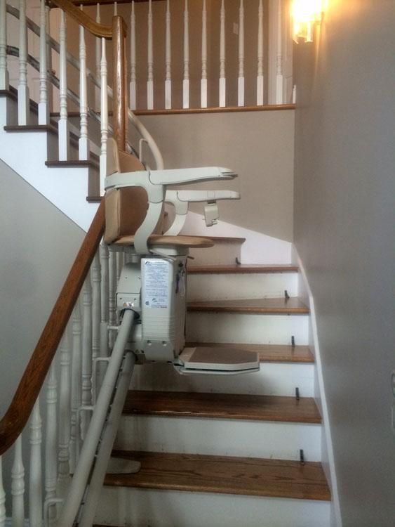 Fauteuil monte-escalier sur un escalier intérieur étroit avec des marches en bois et une rampe blanche