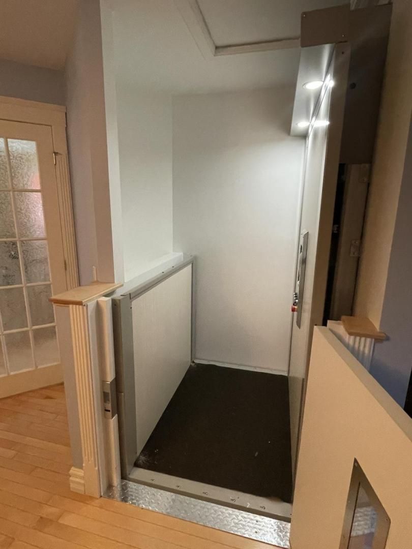 Petit monte-escalier intérieur avec siège gris, placé à côté d'une porte et de murs blancs dans un couloir.