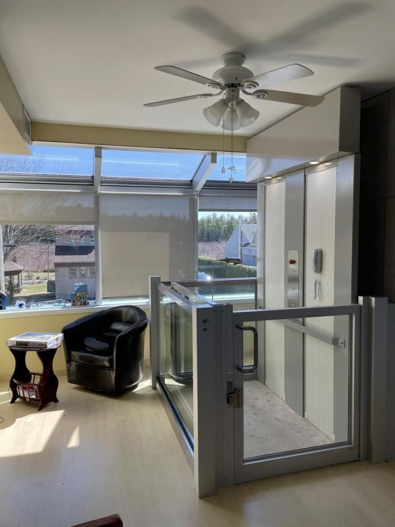 Salon lumineux avec fenêtres, ventilateur de plafond et porte-fenêtre donnant sur un balcon avec vue extérieure