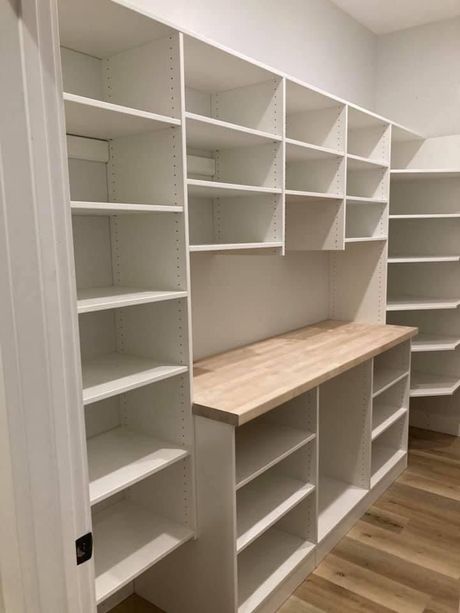 White pantry with many shelves, wooden countertop, and wood floor.
