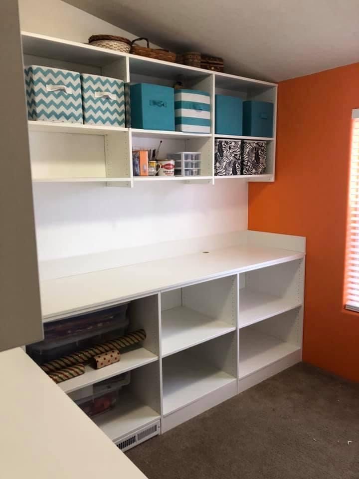 White storage unit with built-in desk, shelves, and colorful bins against orange wall; craft room.