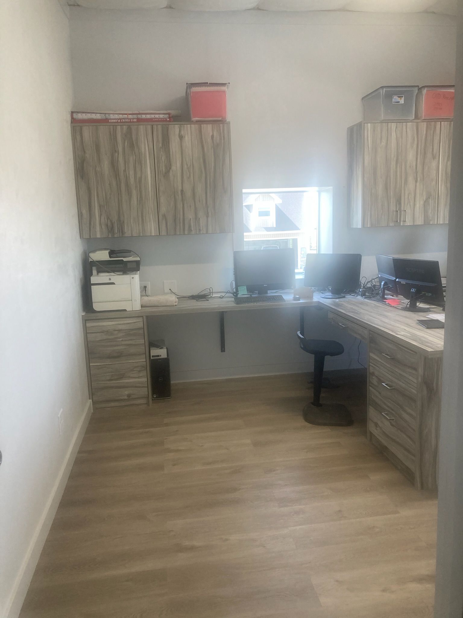 Office with wood-look cabinets, desk with two monitors, printer, and desk chair.