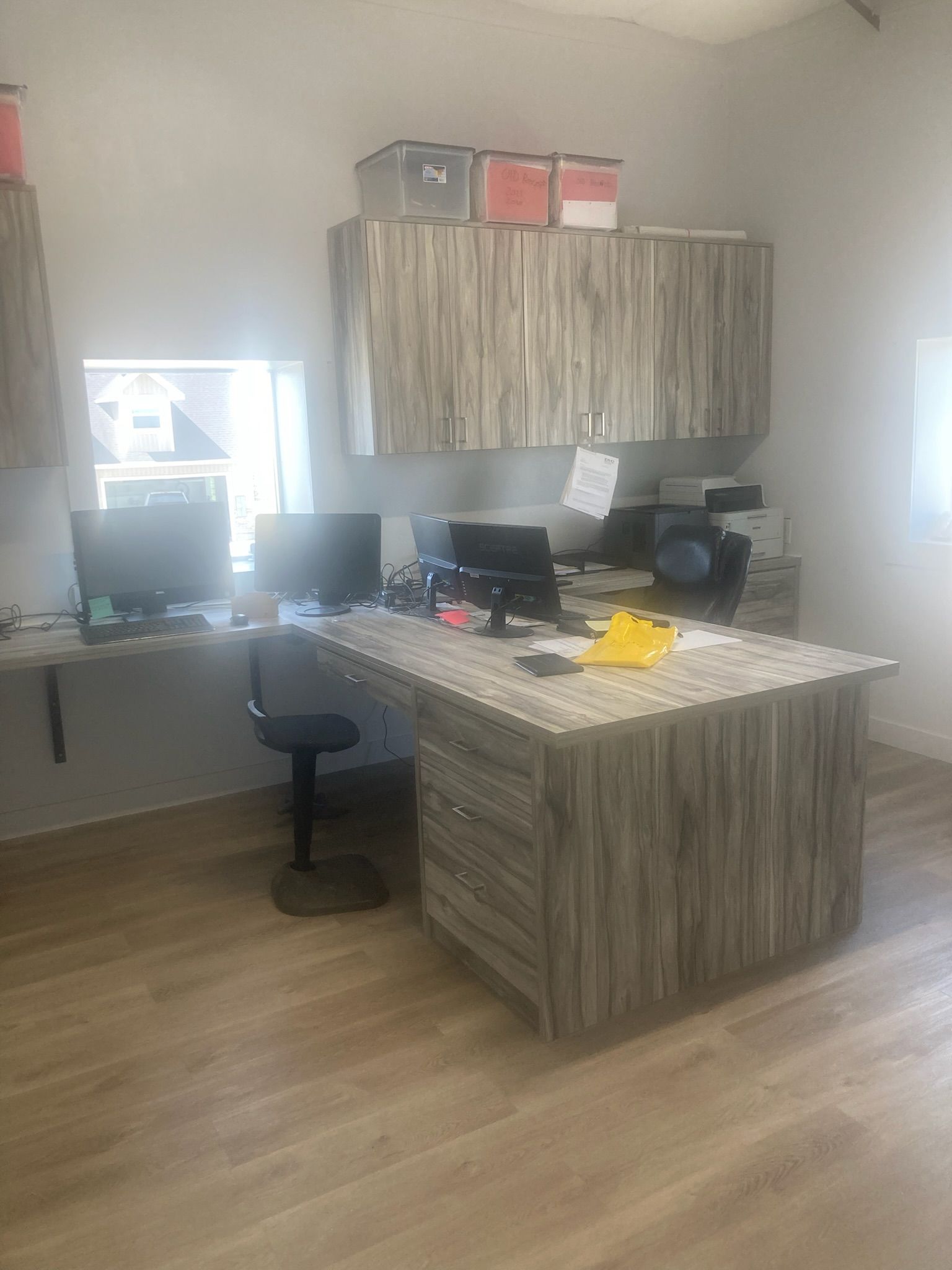 Office space with a desk, computer monitors, cabinets, and a chair. The desk and cabinets have a wooden look.