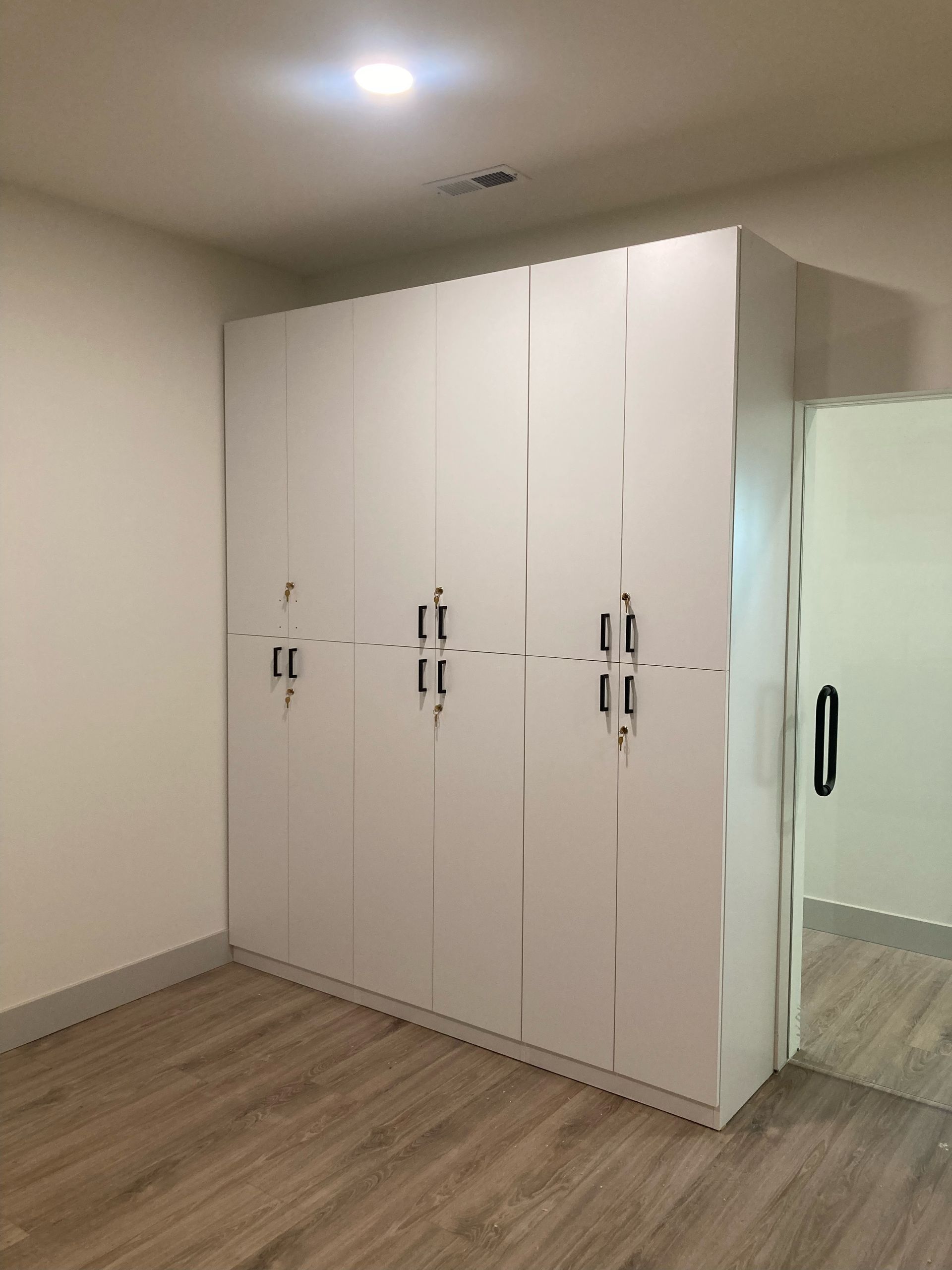 White closet with dark handles in a room with wood-look flooring and a doorway.