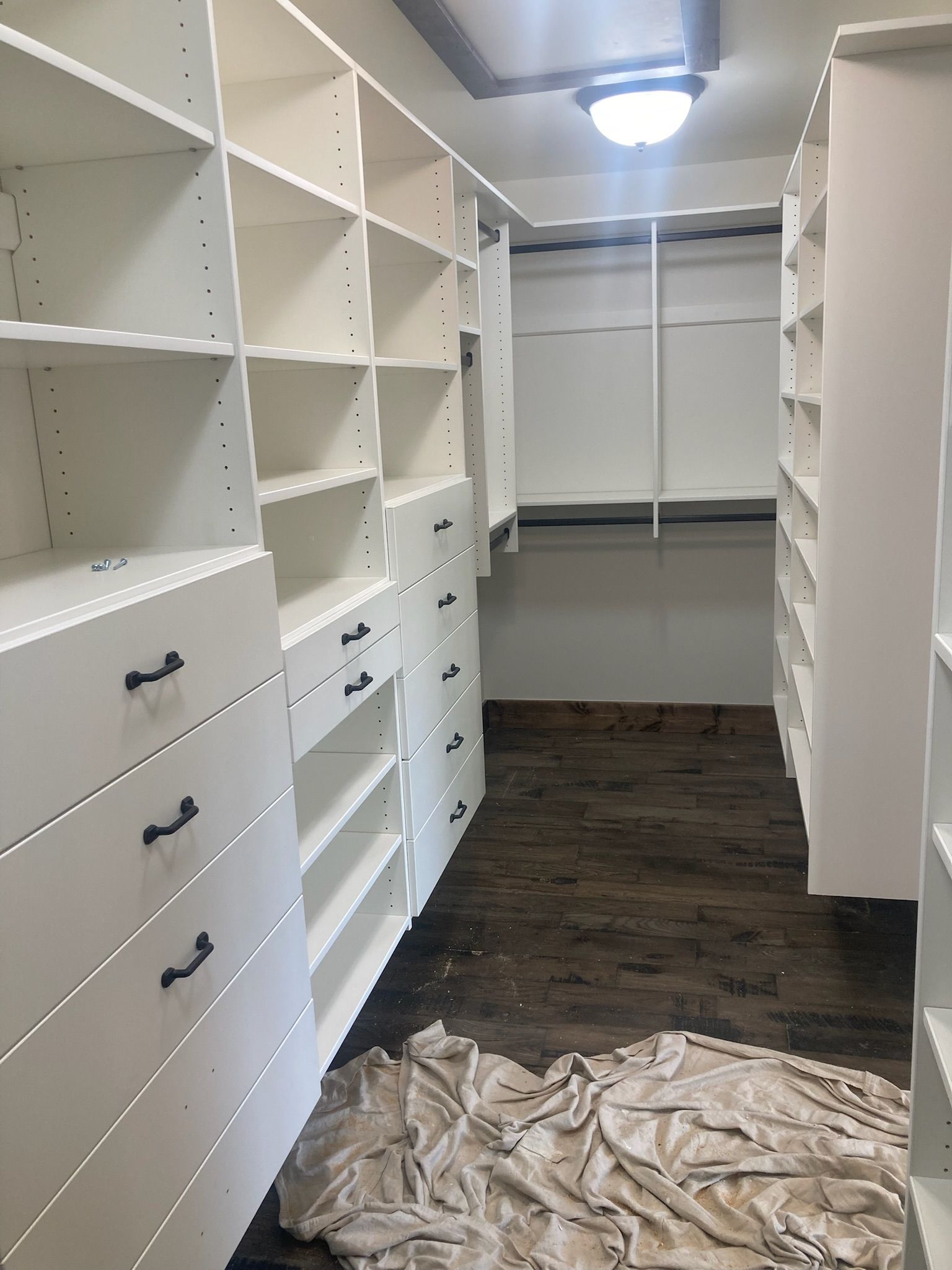 White closet with drawers and shelves; a white blanket lies on the dark brown floor.