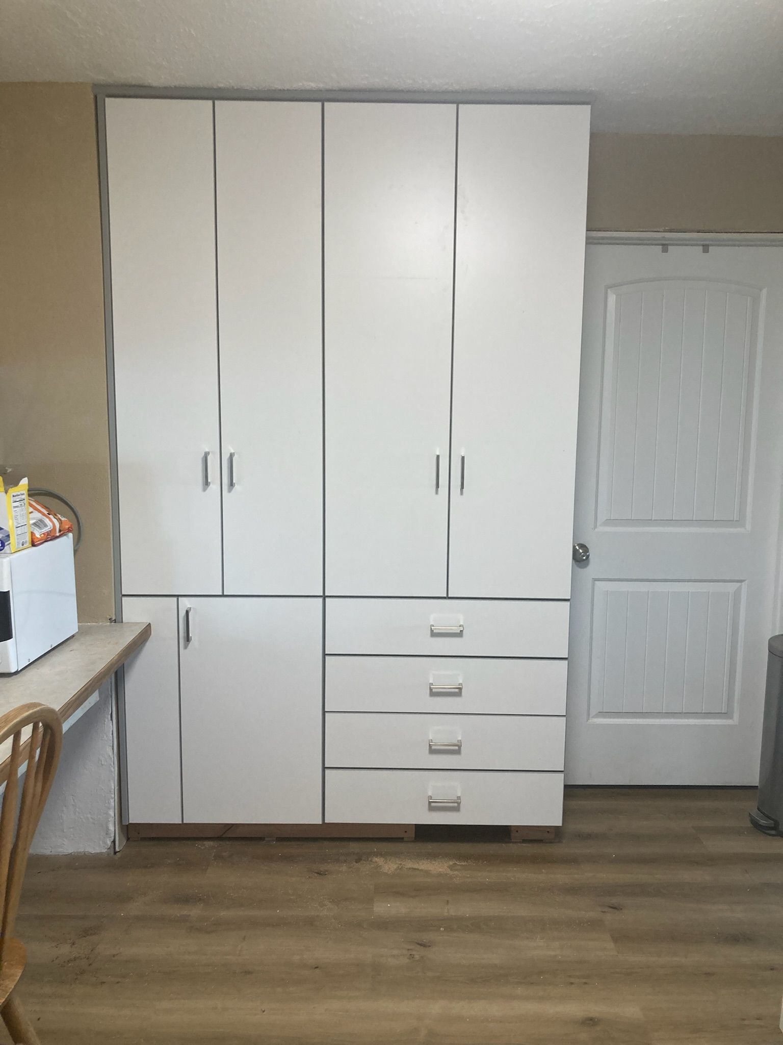 White storage cabinet with drawers and doors next to a white door, set in a room with wood-like flooring.