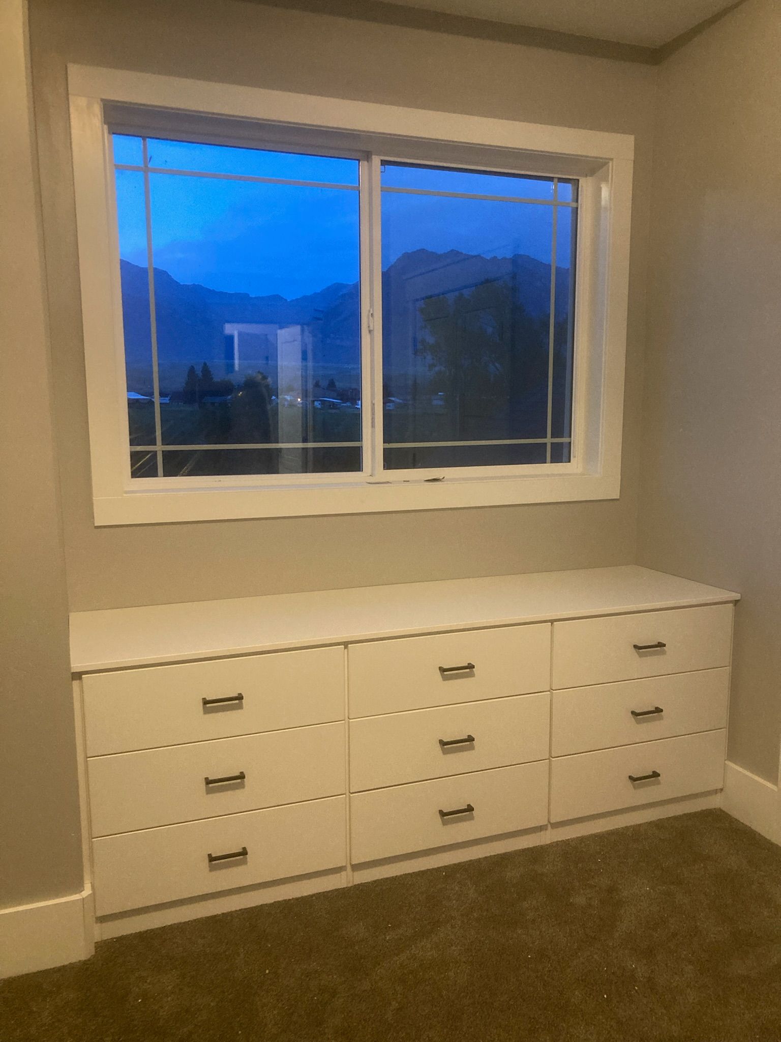 White dresser beneath a window with a view of mountains. The sky is blue.