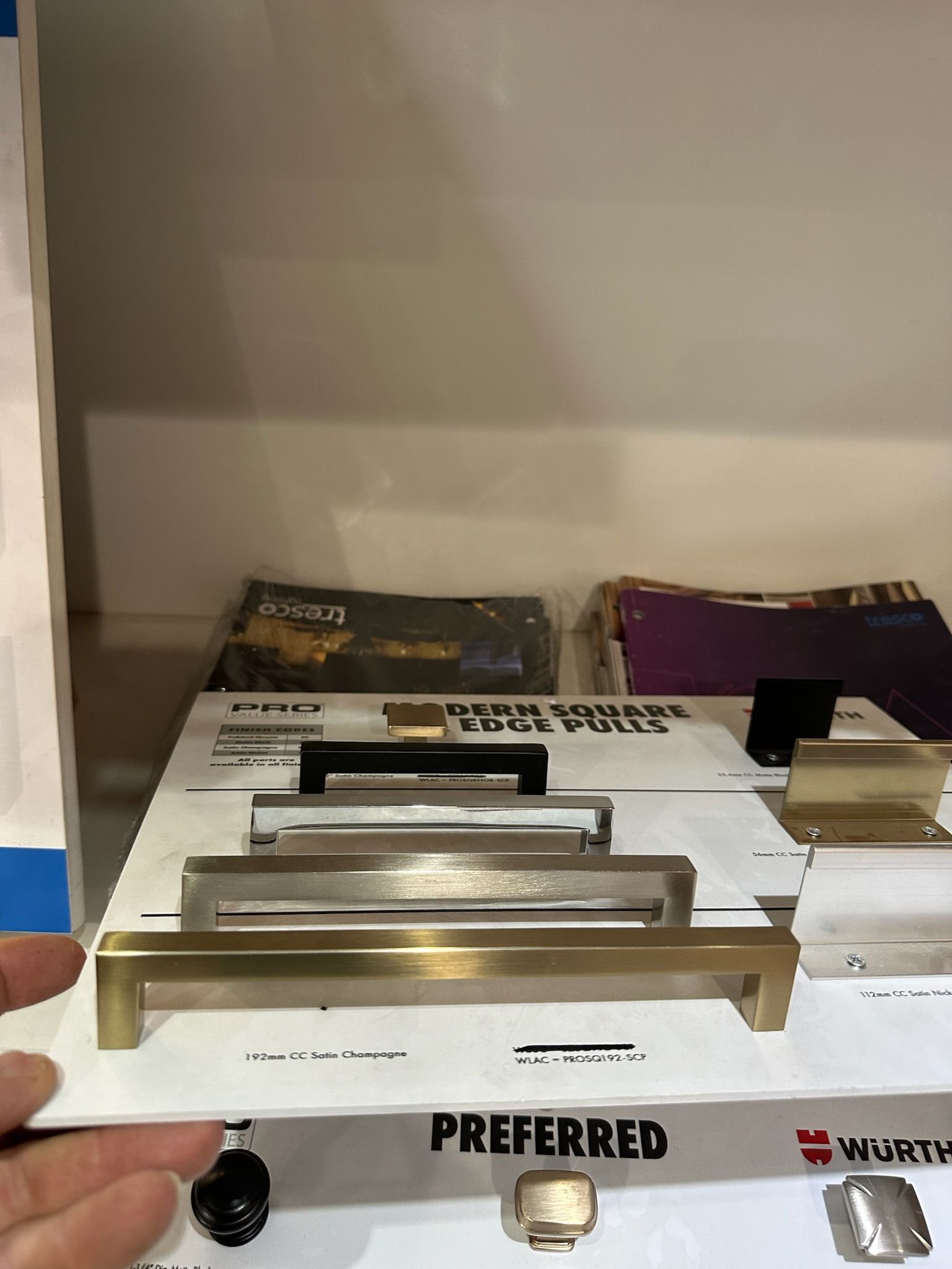 A hand holding a display board of gold and silver cabinet hardware samples, labeled 