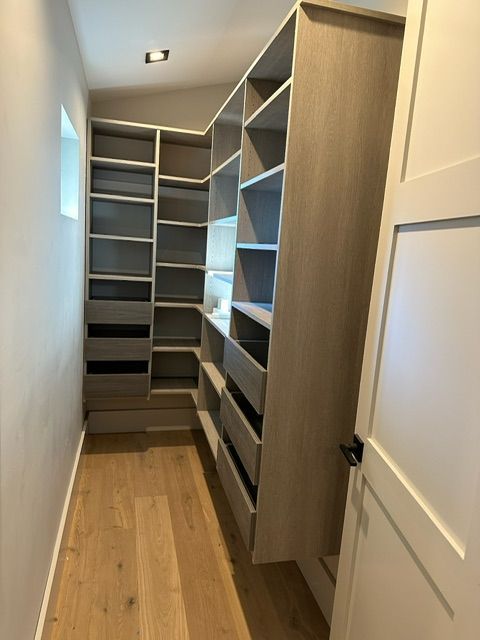 A walk-in closet with built-in light brown wooden shelves and drawers. Light wood floor.