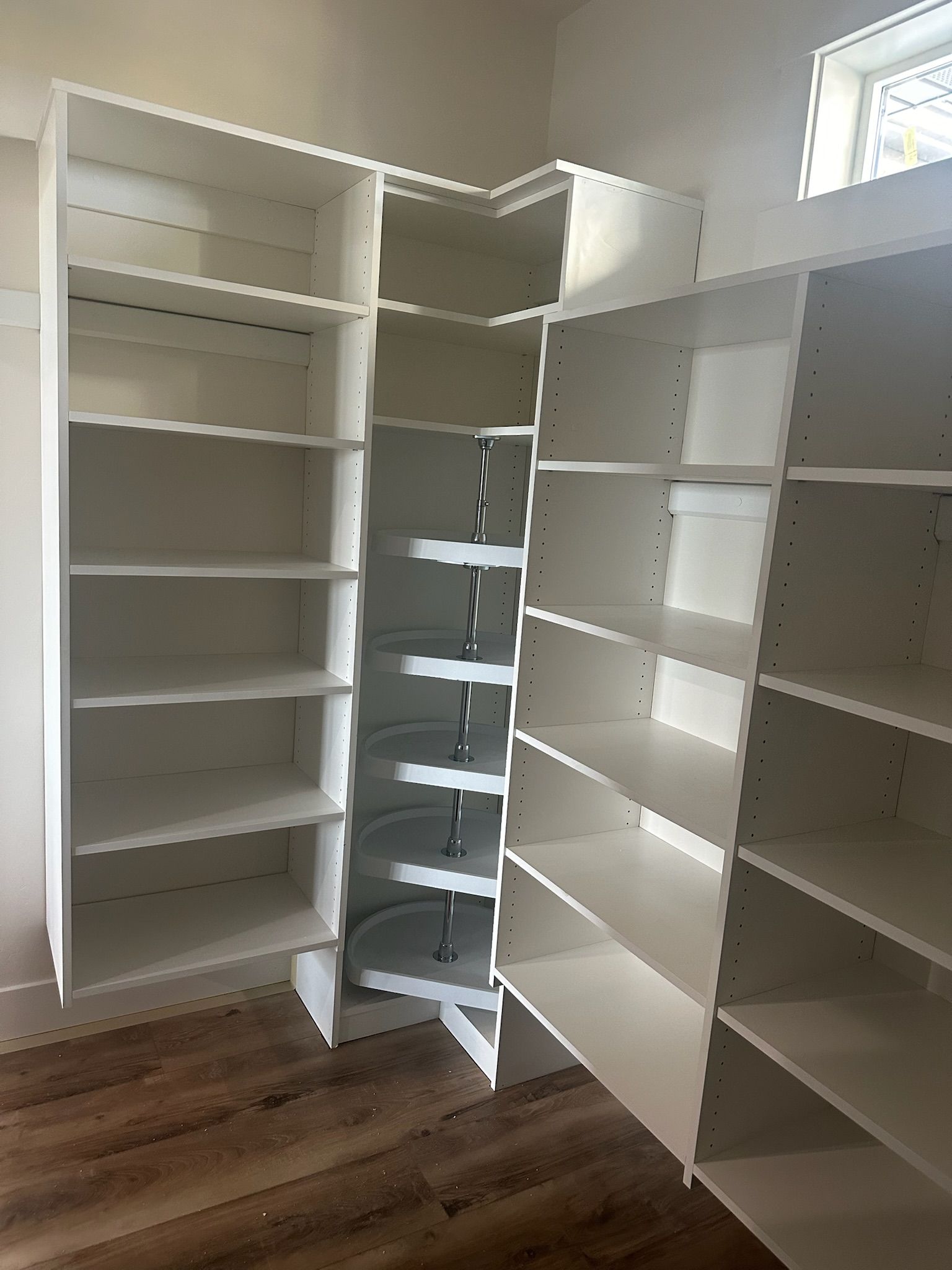 White built-in pantry shelving with a rotating corner unit, open, on a wood floor.