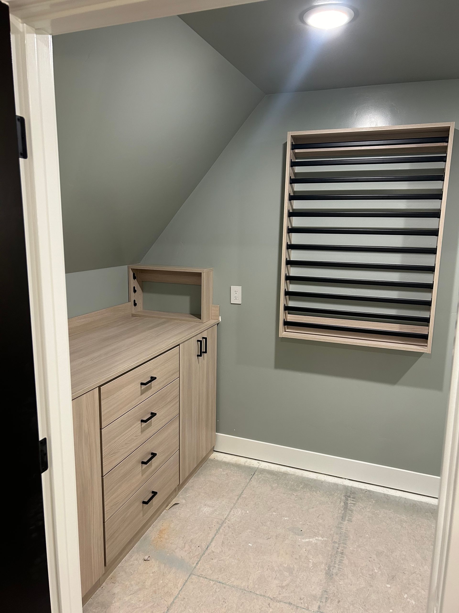 Small, custom-built closet with built-in drawers, countertop, and a shelving unit, all in light wood.