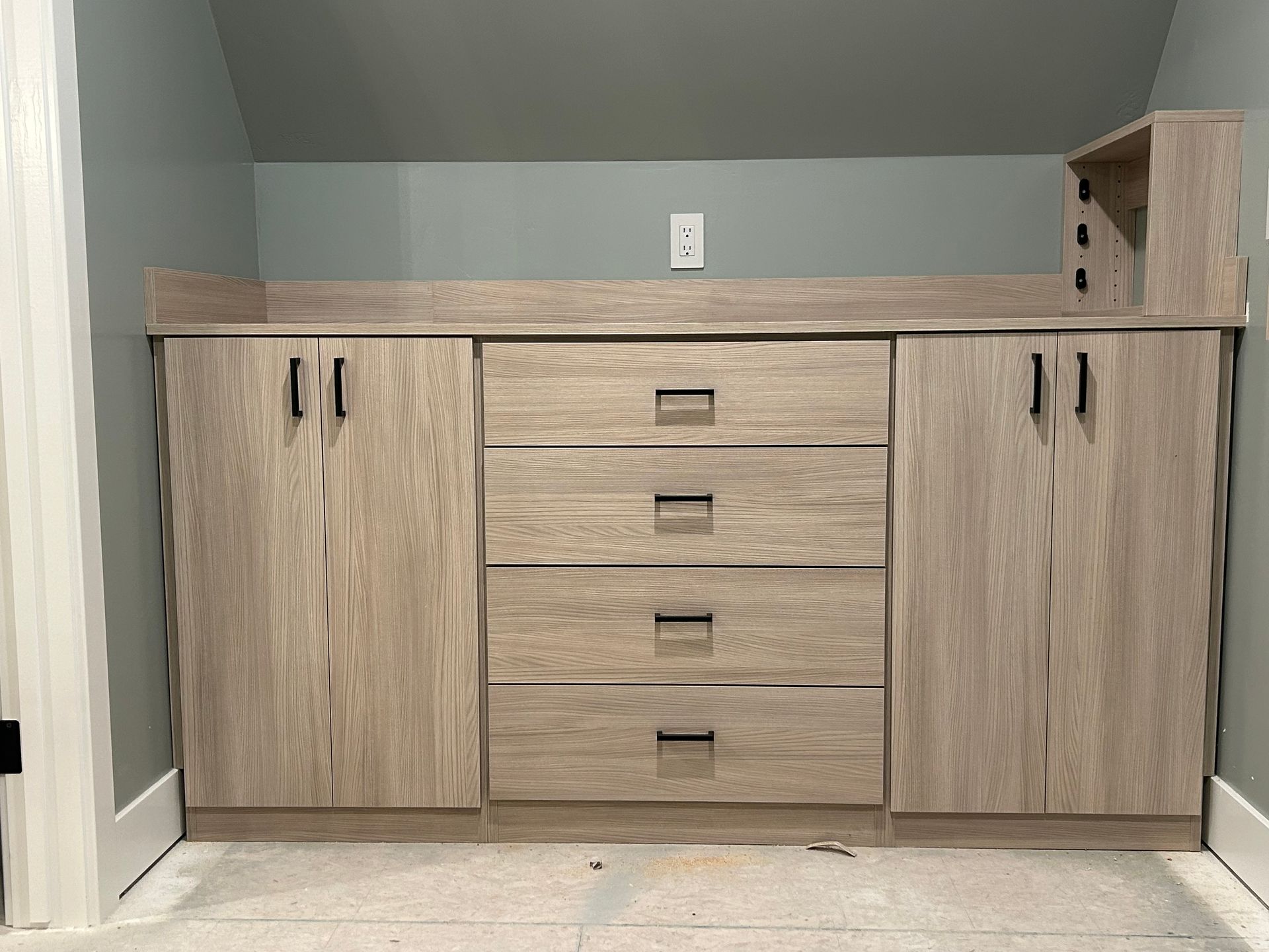 Wooden cabinet unit with doors, drawers, and shelf against a blue-green wall.