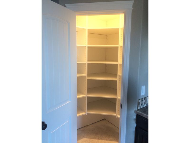 White pantry with built-in shelves. Door is open. Interior lit with warm light.