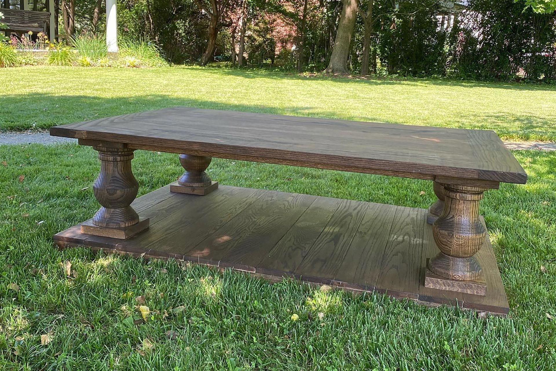 Wooden outdoor coffee table with ornate legs, set on a wood base, on a grassy lawn.