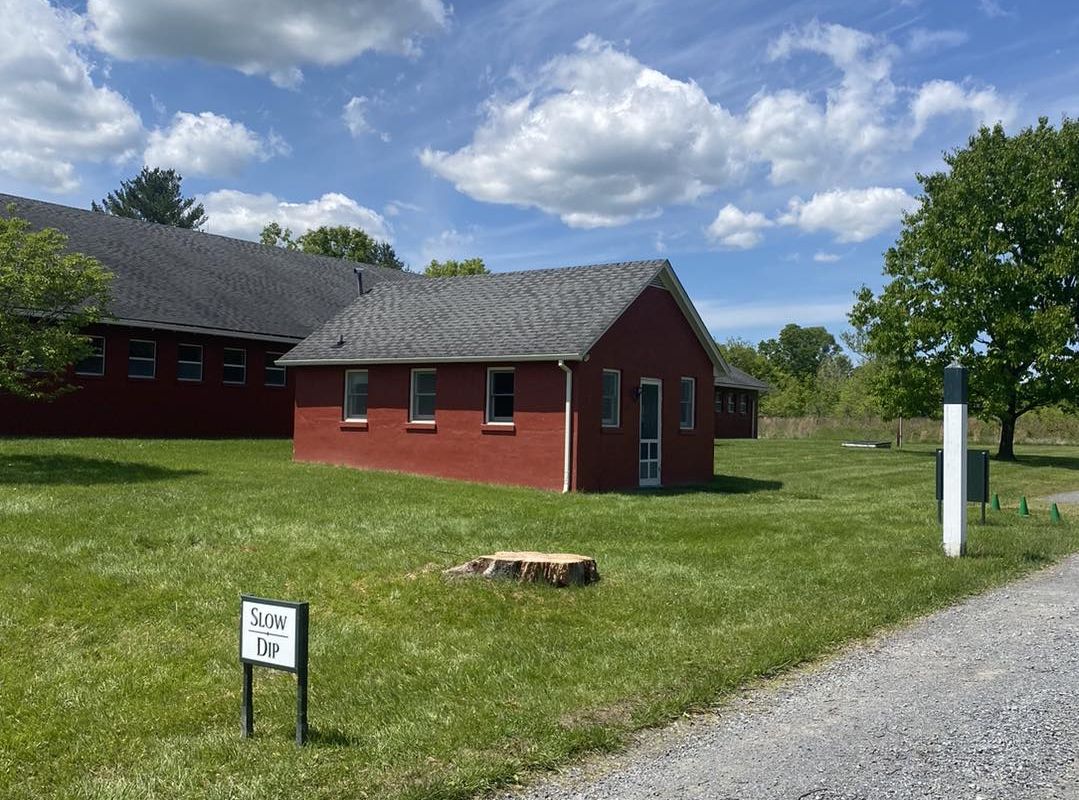 Red building with gray roof sits on green grass under a blue sky.
