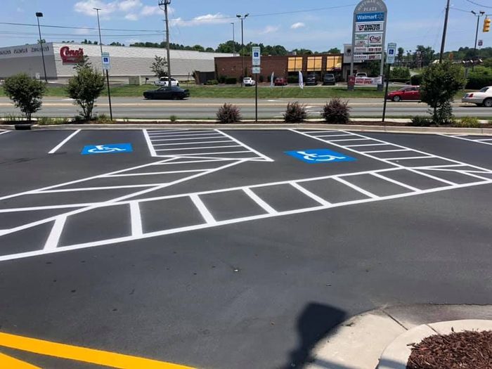 Two freshly painted blue handicap parking symbols with white striped access aisles in an asphalt parking lot.