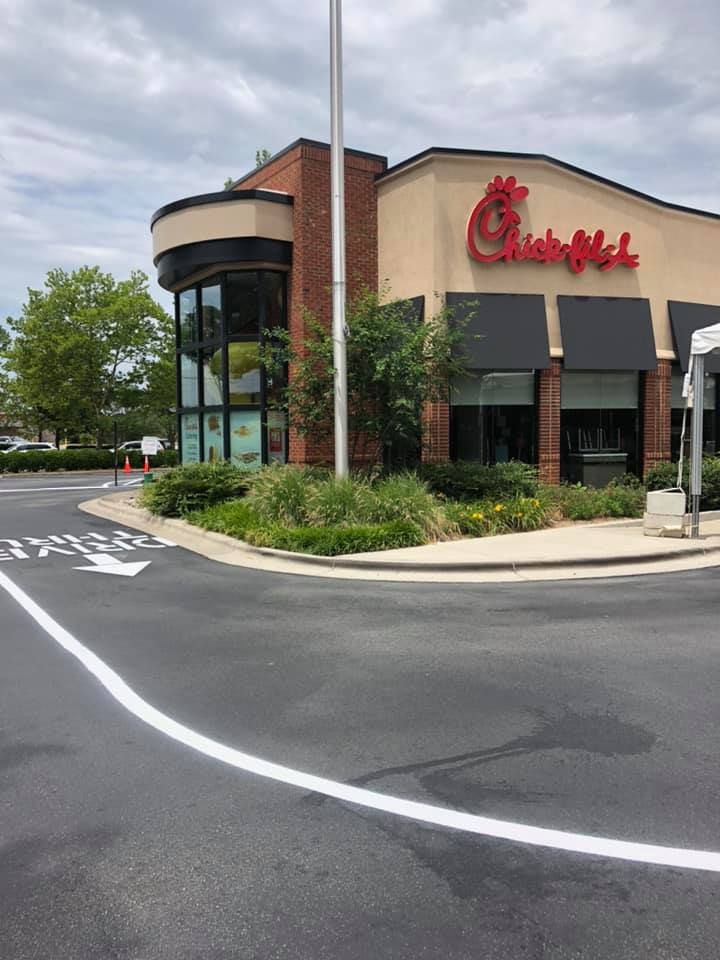 A Chick-fil-A restaurant exterior with a drive-thru lane painted on the asphalt under a cloudy sky.
