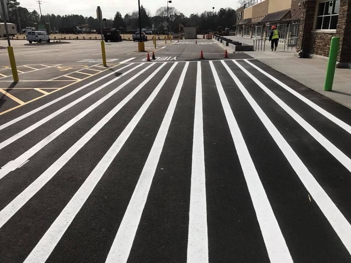 Freshly painted white stripes for an accessible crosswalk in a parking lot next to a building.