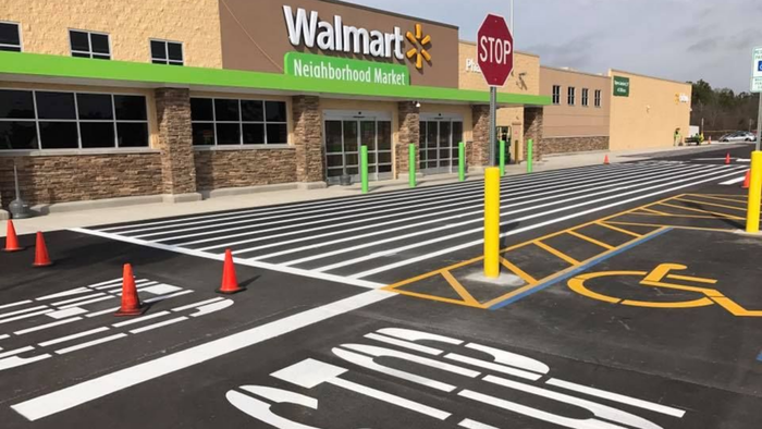 A Walmart Neighborhood Market entrance with a striped crosswalk, safety cones, and an accessible parking space.