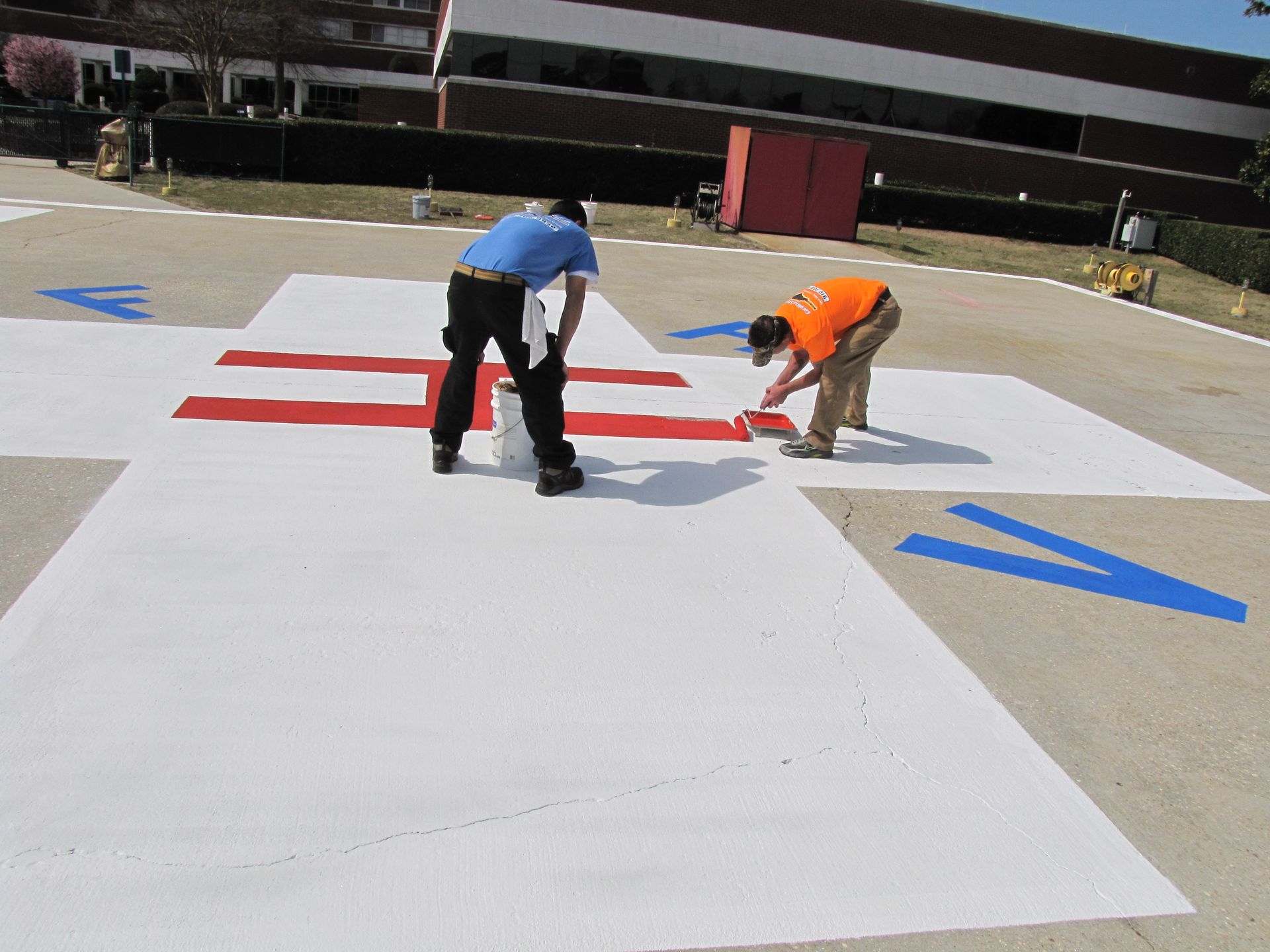 Two workers painting red markings on a white parking lot surface outdoors