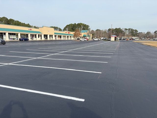 Empty parking lot beside a strip mall with fresh dark asphalt and white parking lines.